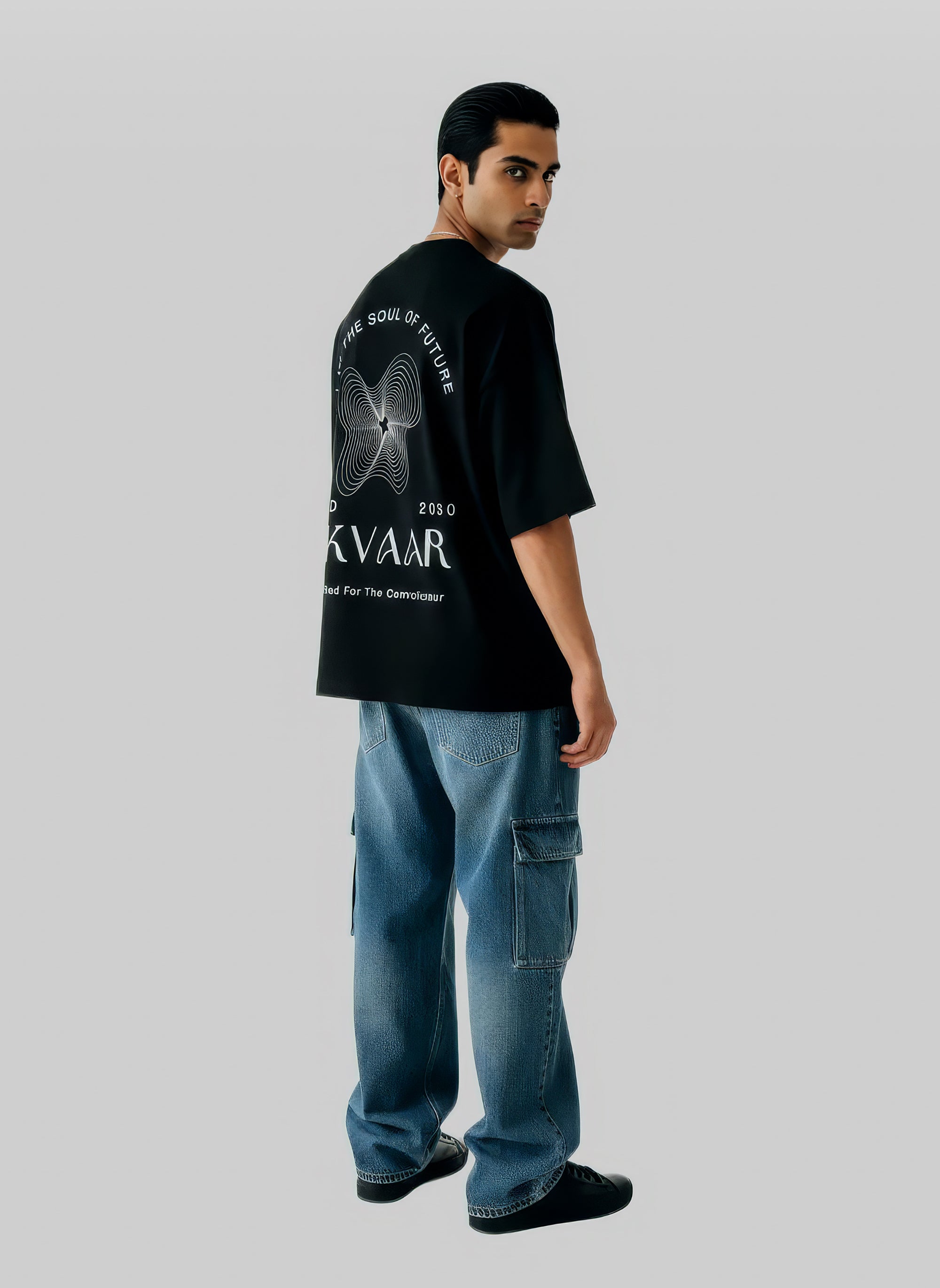 Man wearing a black t-shirt with branding and blue jeans on a gray background