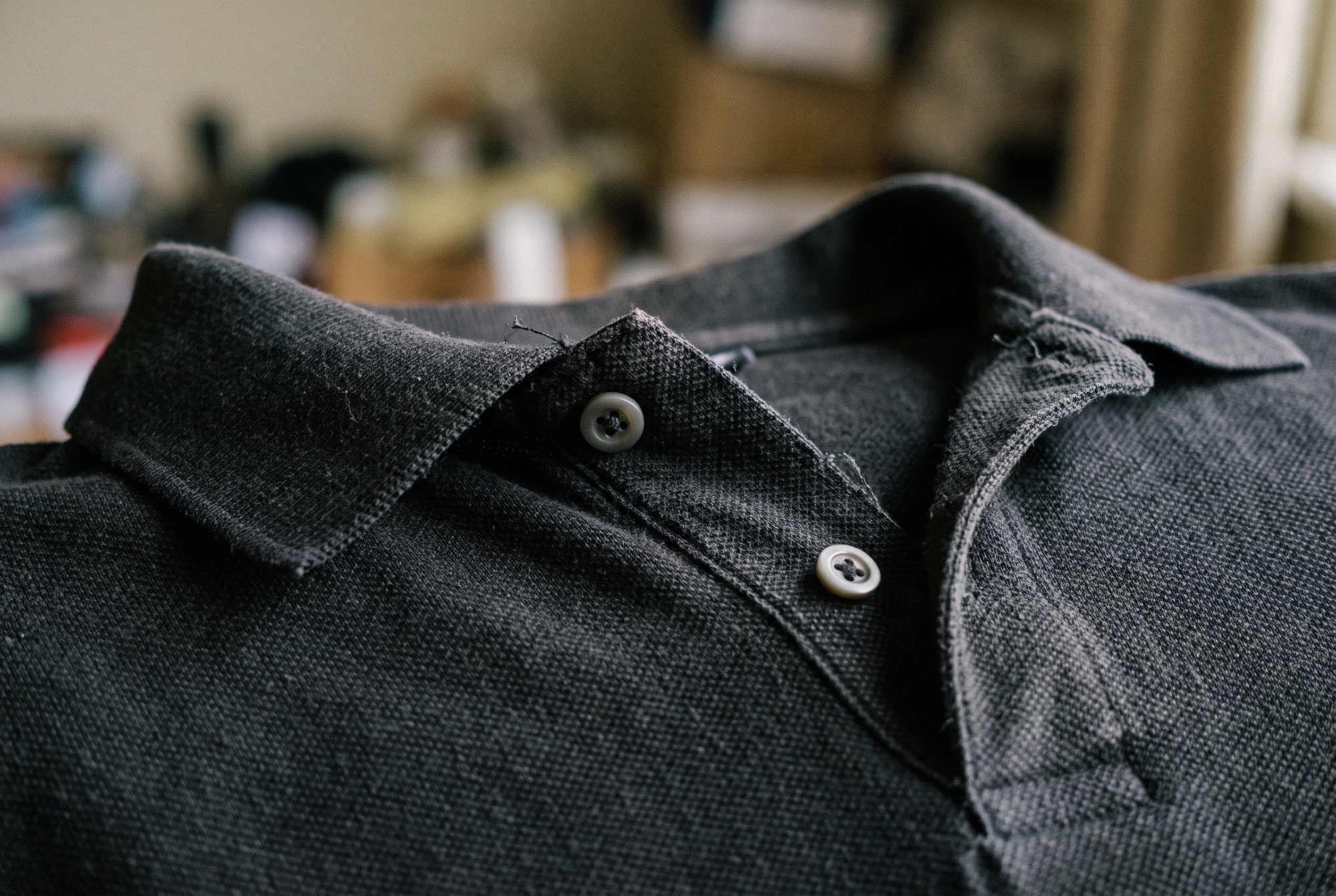 Extreme close-up of black piqué knit fabric texture with a ribbed collar edge and a polo placket with two buttons